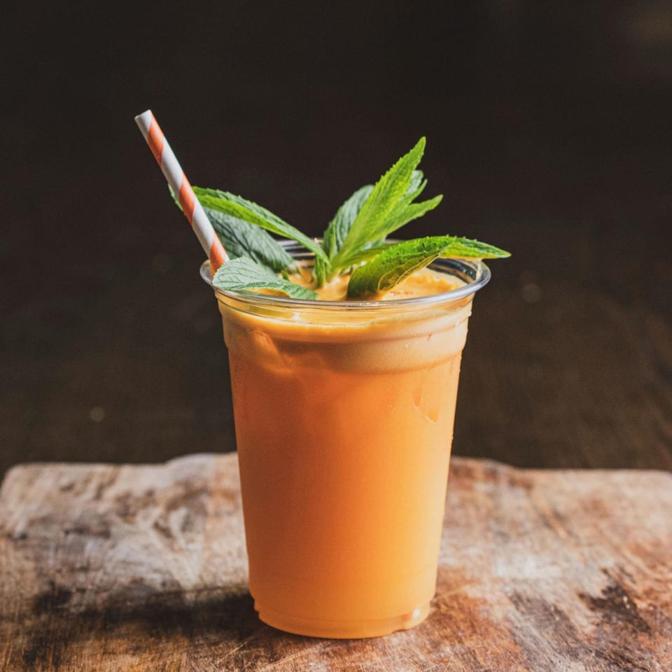 Thai iced tea in a clear plastic cup with a striped straw and mint garnish.